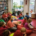 Grupa dzieci w bibliotece słucha lekarza czytającego książkę