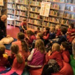 Grupa dzieci w bibliotece słucha strażaka w mundurze
