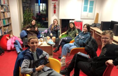 Grupa młodzieży siedzi w bibliotece i rozmawia o książkach